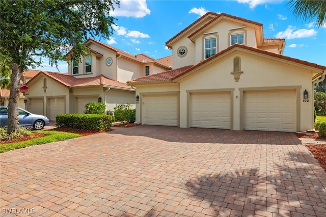 mediterranean / spanish-style home with stucco siding, an attached garage, a tile roof, and decorative driveway