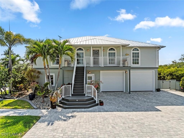 coastal inspired home featuring covered porch, a standing seam roof, stairway, decorative driveway, and an attached garage