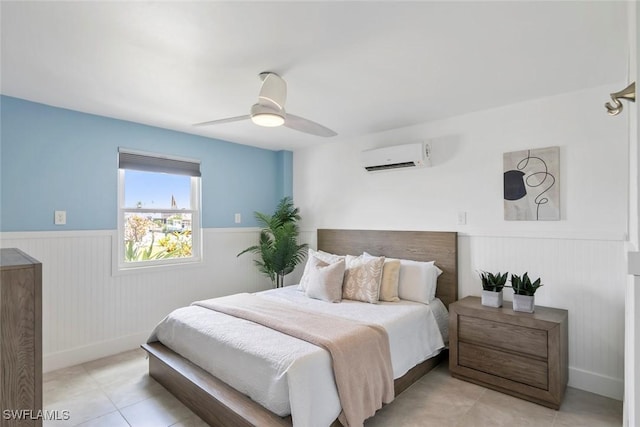 tiled bedroom with ceiling fan, wainscoting, baseboards, and a wall mounted air conditioner