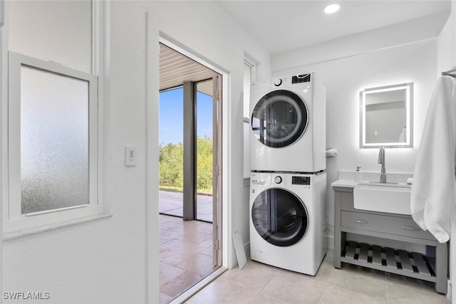 clothes washing area with laundry area, a sink, light tile patterned floors, and stacked washer / dryer