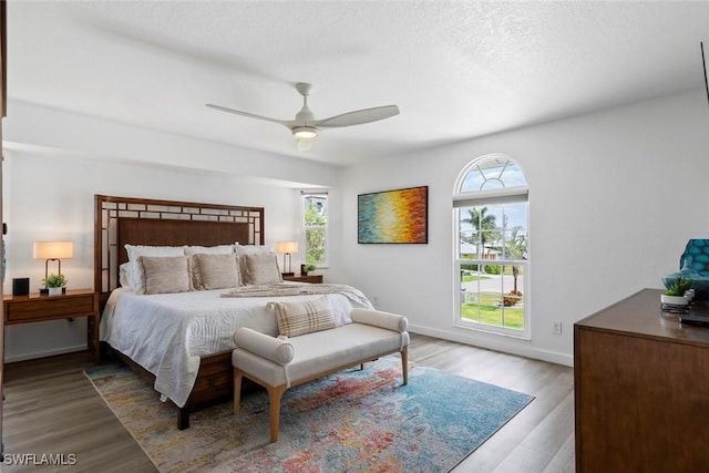 bedroom with baseboards, ceiling fan, multiple windows, and wood finished floors