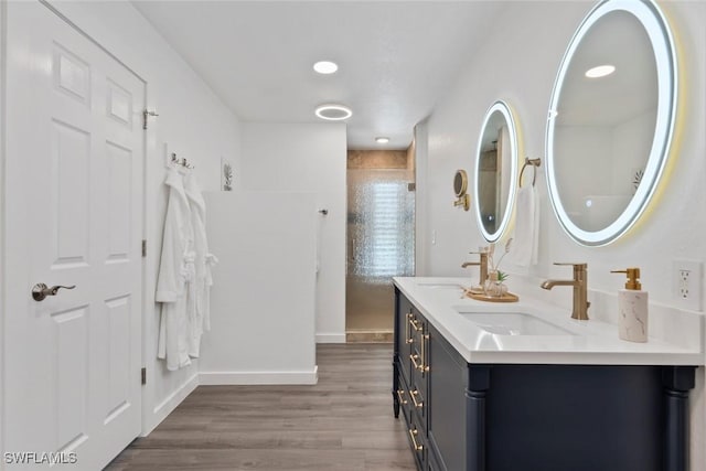 bathroom with double vanity, tiled shower, a sink, and wood finished floors
