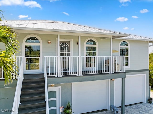entrance to property featuring a garage, a standing seam roof, covered porch, driveway, and metal roof