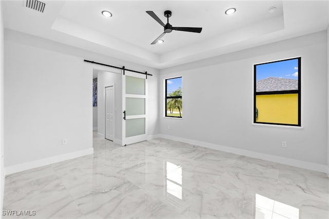 unfurnished bedroom featuring a tray ceiling, marble finish floor, a barn door, and visible vents
