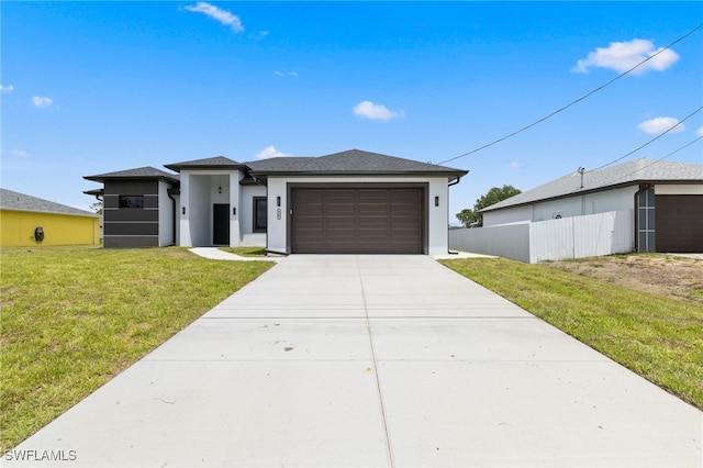 prairie-style home with a front yard, a garage, fence, concrete driveway, and stucco siding