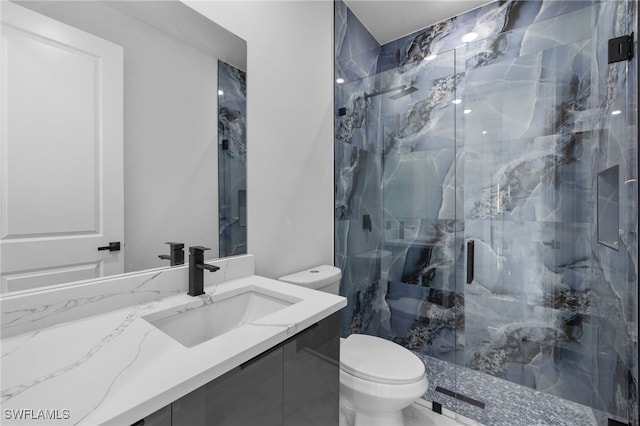 bathroom featuring toilet, a marble finish shower, and vanity