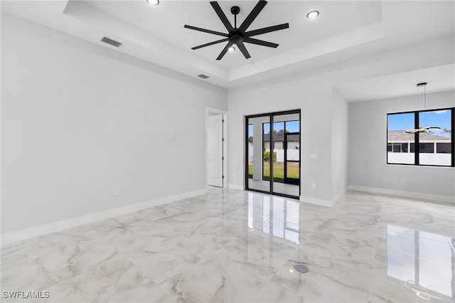 unfurnished room with a tray ceiling, visible vents, plenty of natural light, and marble finish floor