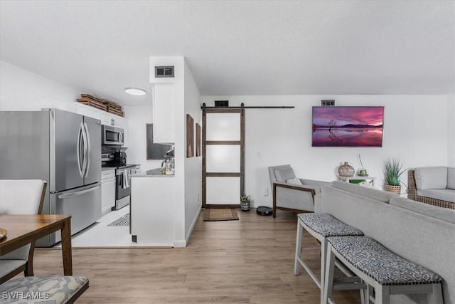 kitchen with stainless steel appliances, a barn door, light wood-style flooring, white cabinetry, and open floor plan
