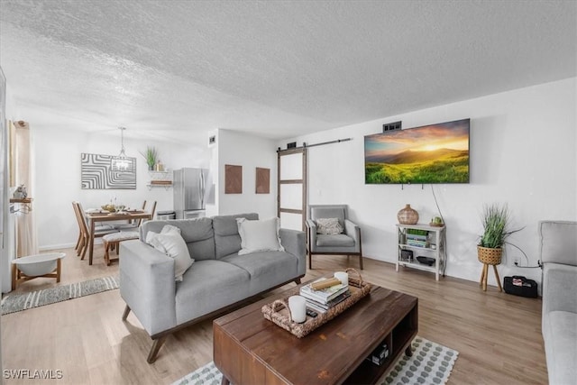 living room featuring a textured ceiling, a barn door, light wood finished floors, and a chandelier