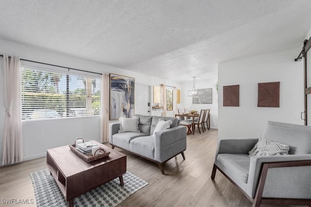 living room featuring a textured ceiling, healthy amount of natural light, light wood-type flooring, and a chandelier