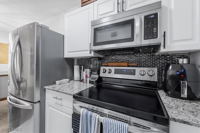 kitchen with appliances with stainless steel finishes, white cabinets, and tasteful backsplash