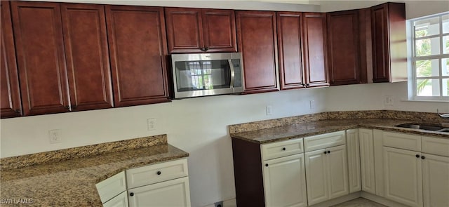315 Cleveland Ave, Lehigh Acres, FL 33936 - kitchen featuring a sink, dark stone counters, stainless steel microwave, and reddish brown cabinets