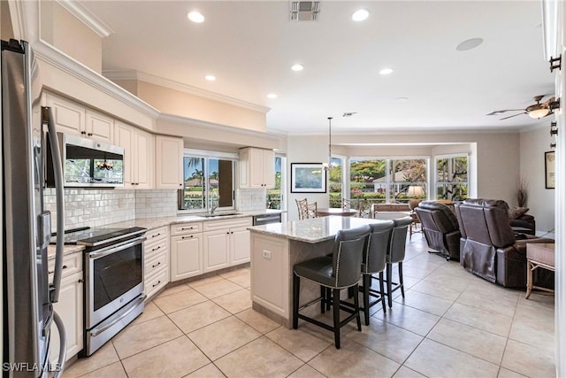 kitchen with appliances with stainless steel finishes, a sink, open floor plan, visible vents, and ornamental molding