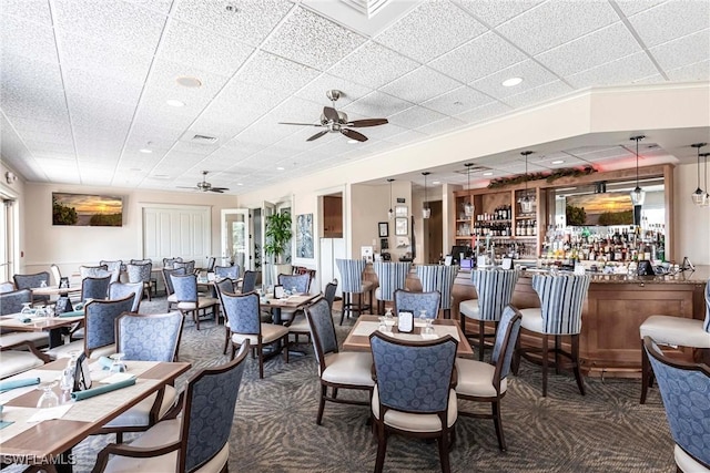 dining space featuring a ceiling fan, plenty of natural light, a bar, and carpet