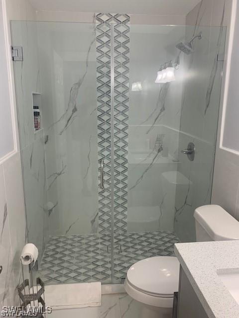 full bathroom with toilet, a marble finish shower, and vanity