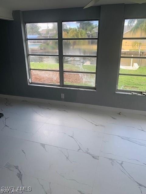 spare room featuring marble finish flooring, a water view, and plenty of natural light