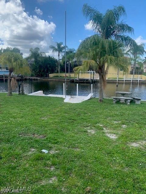 view of green lawn with a water view and a dock