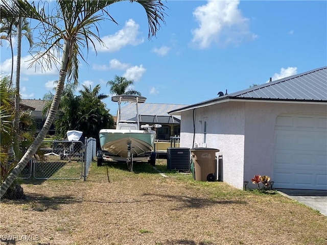view of side of home with stucco siding, central AC unit, fence, metal roof, and a garage