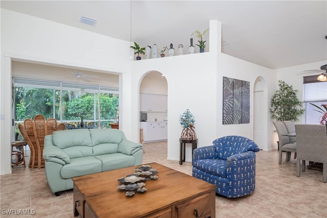 living area with light tile patterned flooring, visible vents, a ceiling fan, and arched walkways