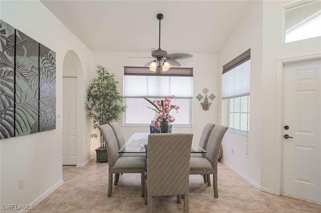 dining area featuring arched walkways, baseboards, ceiling fan, and vaulted ceiling