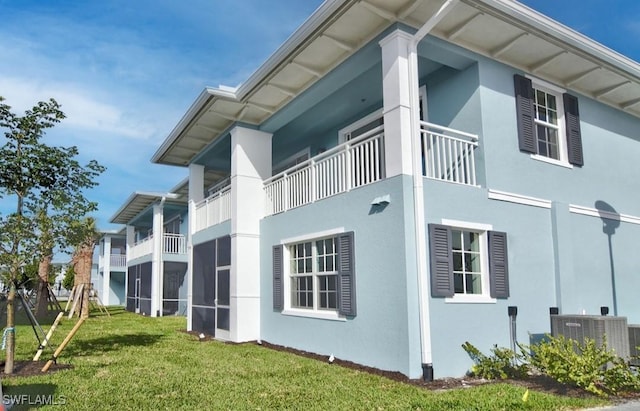 view of side of property featuring central AC unit, stucco siding, and a yard