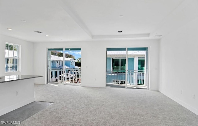 unfurnished living room featuring carpet floors, a raised ceiling, baseboards, and visible vents