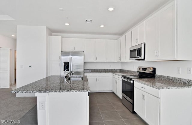 kitchen featuring visible vents, a kitchen island with sink, a sink, stone counters, and appliances with stainless steel finishes