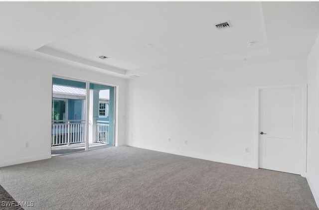 unfurnished room with a tray ceiling, visible vents, baseboards, and carpet