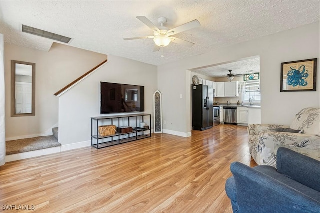 239 Leawood Cir, Naples, FL 34104 - living room featuring light wood-style floors, a textured ceiling, a ceiling fan, stairs, and baseboards
