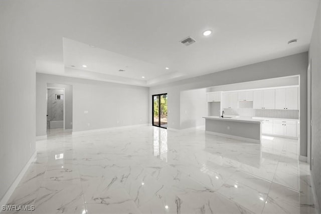 203 E 10th St, Lehigh Acres, FL 33972 - unfurnished living room featuring a sink, baseboards, a tray ceiling, recessed lighting, and light marble finish floors