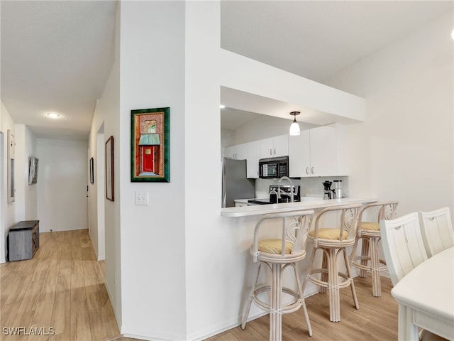 935 New Waterford Dr Unit F204, Naples, FL 34104 - kitchen featuring a breakfast bar, freestanding refrigerator, light wood-style flooring, black microwave, and stove