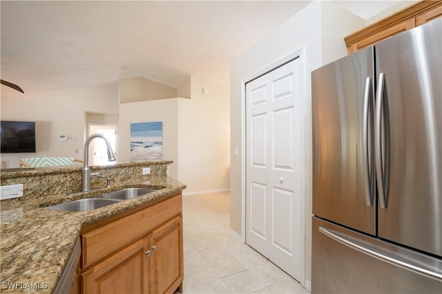 kitchen featuring freestanding refrigerator, lofted ceiling, light stone counters, a sink, and light tile patterned floors