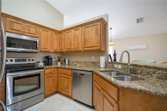 kitchen featuring brown cabinets, a sink, stainless steel appliances, stone counters, and light tile patterned floors