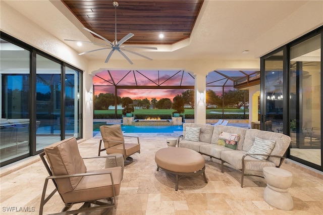 patio terrace at dusk with glass enclosure, an outdoor pool, an outdoor living space, ceiling fan, and a jacuzzi