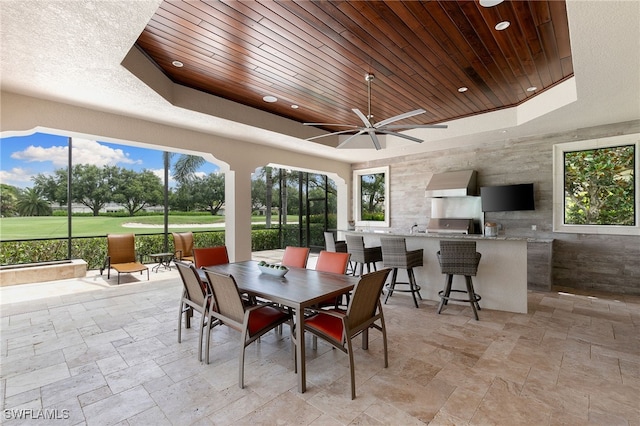 dining area with view of golf course, stone tile flooring, wooden ceiling, a ceiling fan, and a tray ceiling