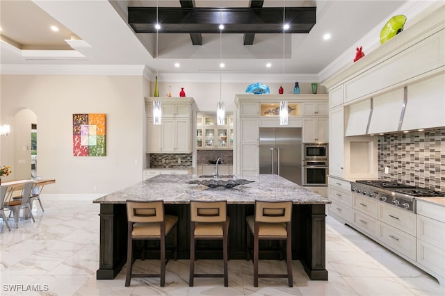 kitchen with crown molding, arched walkways, built in appliances, and a center island with sink