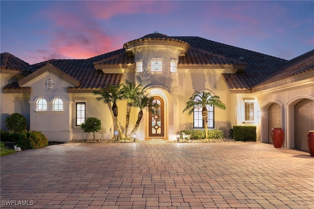 mediterranean / spanish-style house featuring a tile roof, an attached garage, stucco siding, and decorative driveway