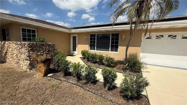 1005 E Penn Rd, Lehigh Acres, FL 33936 - doorway to property featuring an attached garage, roof mounted solar panels, and stucco siding