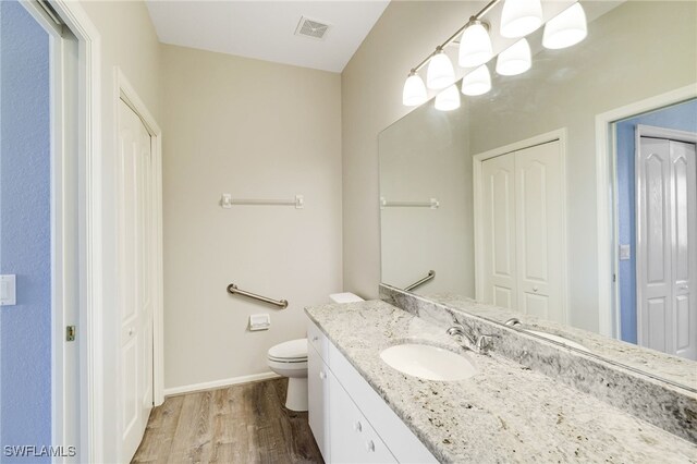 bathroom featuring a closet, wood finished floors, toilet, and vanity