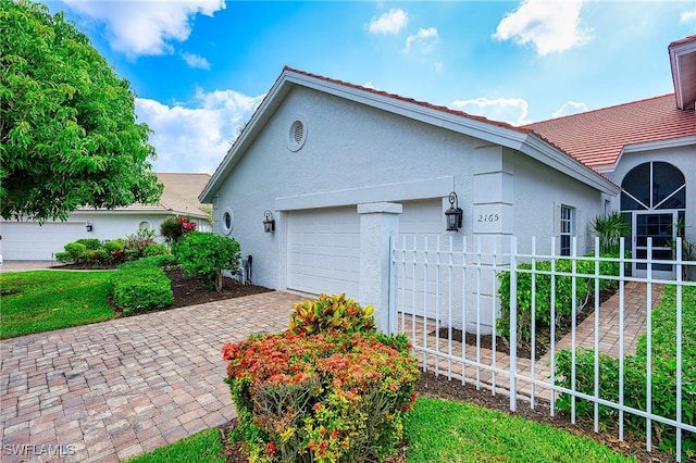 view of side of home featuring stucco siding, a garage, driveway, and a tile roof