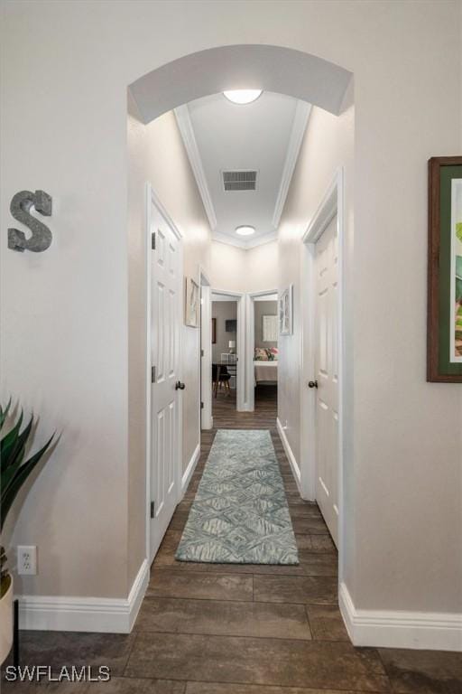 corridor with crown molding, visible vents, wood finished floors, baseboards, and arched walkways