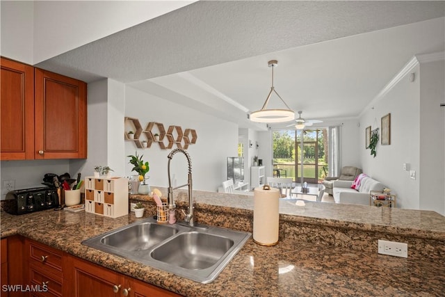 kitchen with a sink, brown cabinets, open floor plan, a ceiling fan, and hanging light fixtures