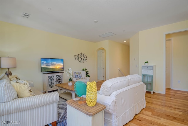 living room with arched walkways, baseboards, visible vents, and light wood-type flooring