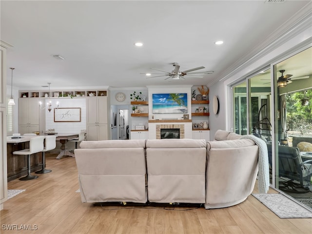 living room with a ceiling fan, ornamental molding, light wood finished floors, and a fireplace