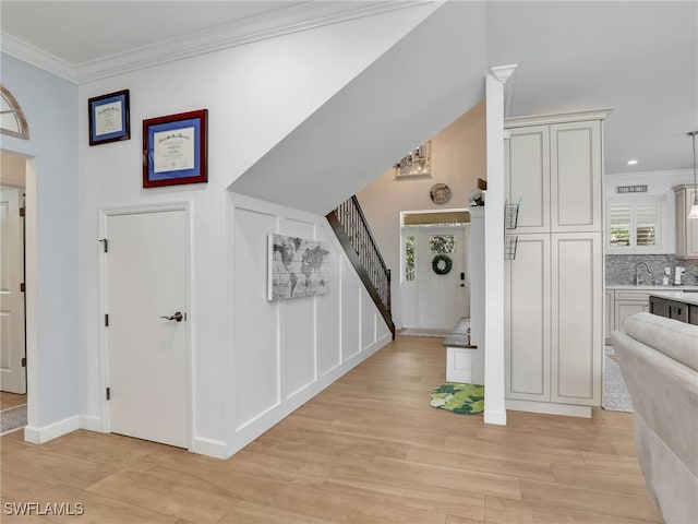 entryway featuring crown molding, an inviting chandelier, stairs, baseboards, and light wood-style floors