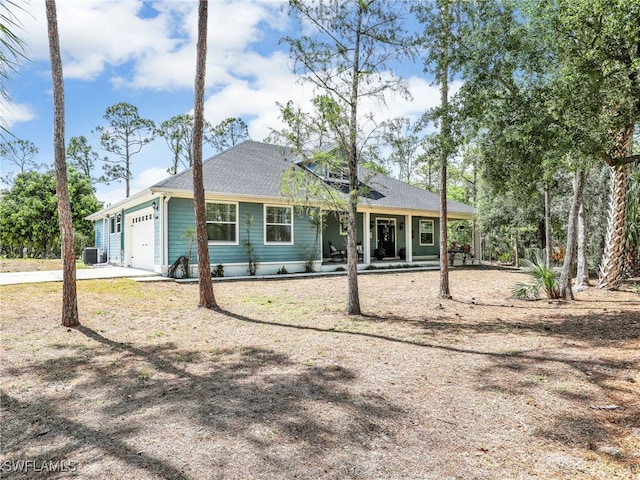view of front of property with covered porch, roof with shingles, central AC unit, a garage, and concrete driveway