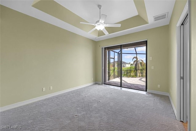carpeted empty room with a raised ceiling, baseboards, and a ceiling fan