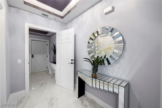 hallway featuring marble finish floor, ornamental molding, visible vents, a tray ceiling, and baseboards