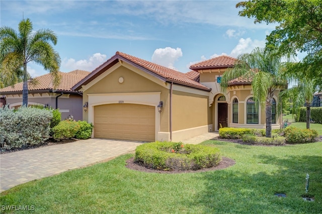 mediterranean / spanish house with an attached garage, stucco siding, a front yard, a tiled roof, and decorative driveway