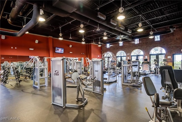 exercise room featuring rail lighting, a high ceiling, and brick wall